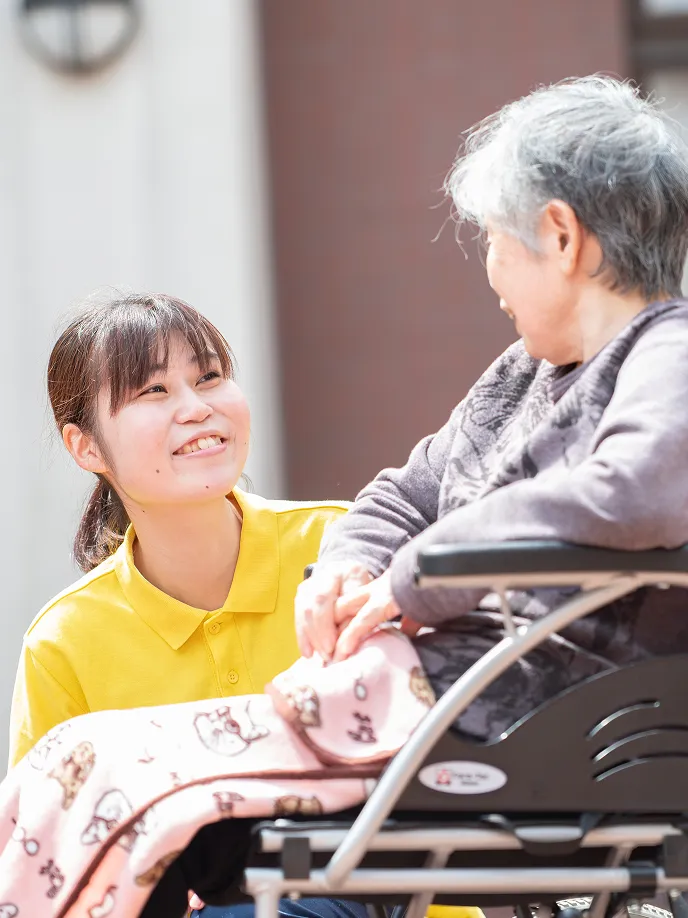 車椅子に座るご利用者と笑顔で手を取り合う介護職員