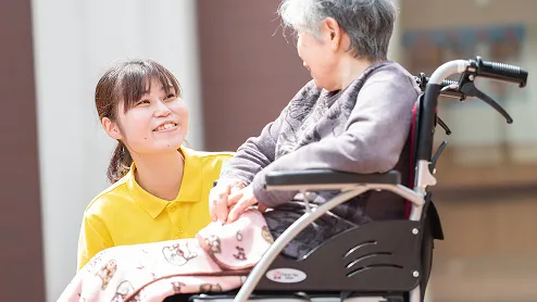 車椅子に座るご利用者と笑顔で手を取り合う介護職員