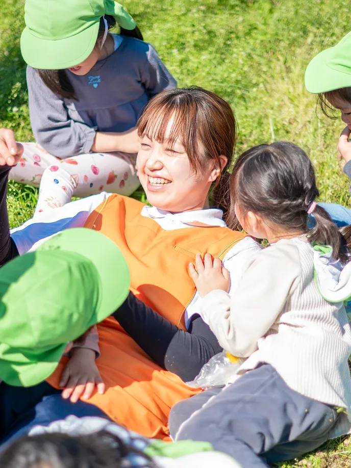 芝生の上で園児たちと笑顔で触れ合う保育士