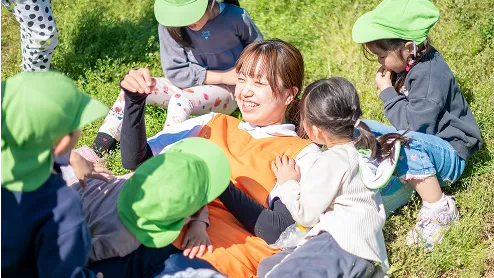 芝生の上で園児たちと笑顔で触れ合う保育士