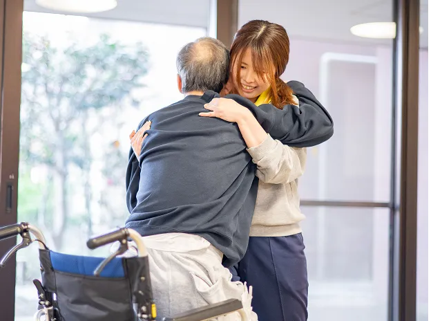 車椅子のご利用者を抱きしめる介護職員