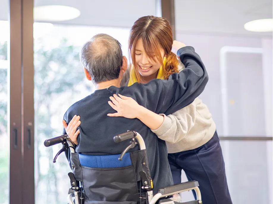 車いすのご利用者に寄り添い体を支える介護職員