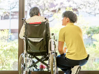 介護職員の男性が車椅子に座る高齢の方に寄り添う様子
